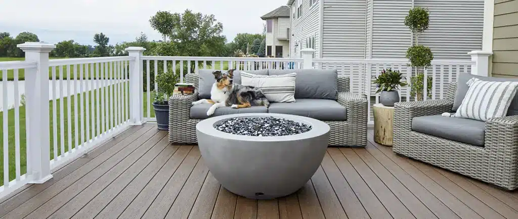 A dog lounges on outdoor furniture in front of a firepit on a composite deck.