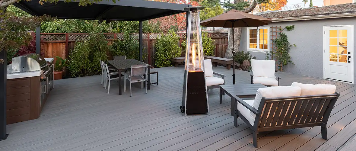 Outdoor deck in the shade at sunset with a heat lamp near two outdoor seating areas.