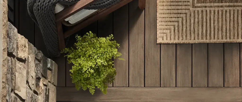 Overhead shot of brown deck with the edges of outdoor furniture, a plant, and a rug in view.