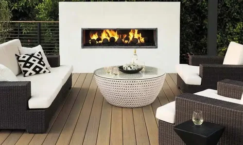 A built-in outdoor fire place is lit on a medium brown deck